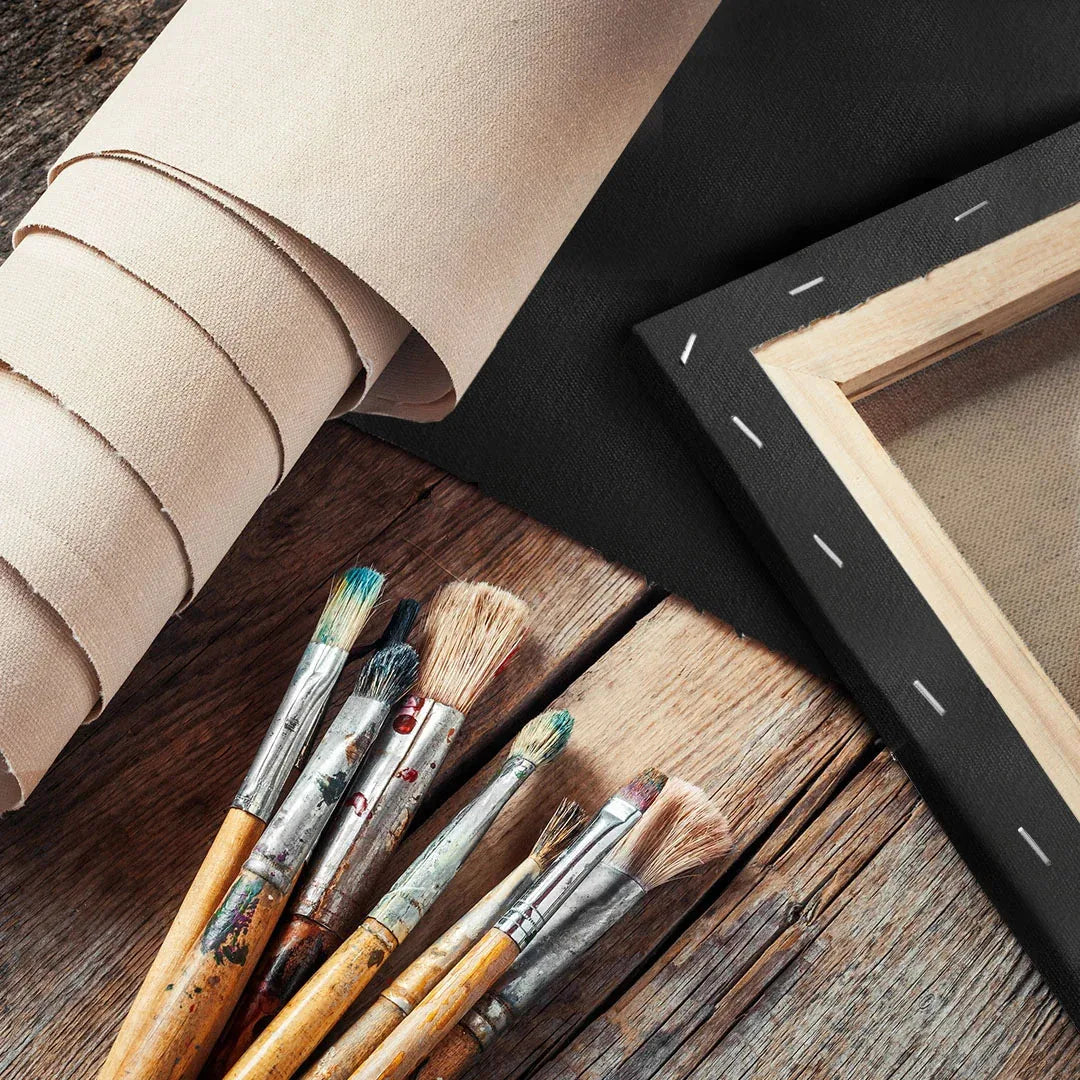 Roll of raw cotton canvas, black primed canvas, and stretched canvas on a spruce frame with staples, beside a set of brushes
