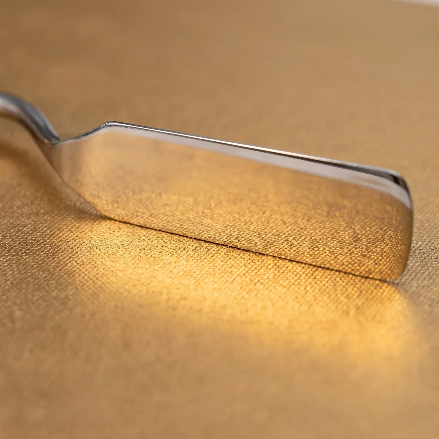 Steel palette knife on the MIDAS gold canvas — the metallic surface reflects in the blade, and the cotton weave is visible beneath the pigment