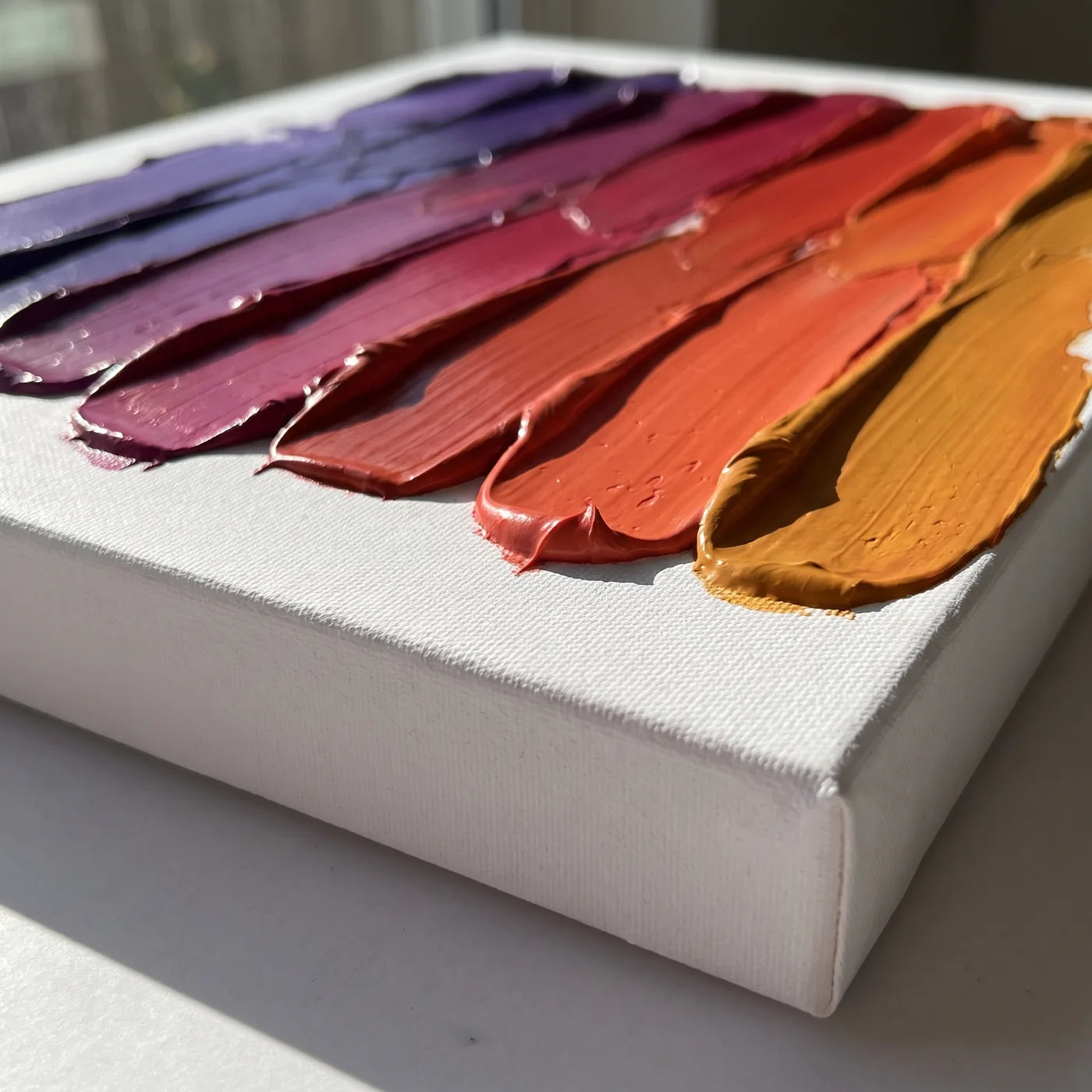 Side edge of the 3D canvas — white side with a frame depth of 4 cm and strips of thick acrylic paint applied with a palette knife, each in a different color, together creating a gradient from purple to amber